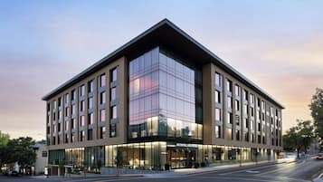 A modern hotel with a prominent glass facade, a flat roof, and a corner entrance.
