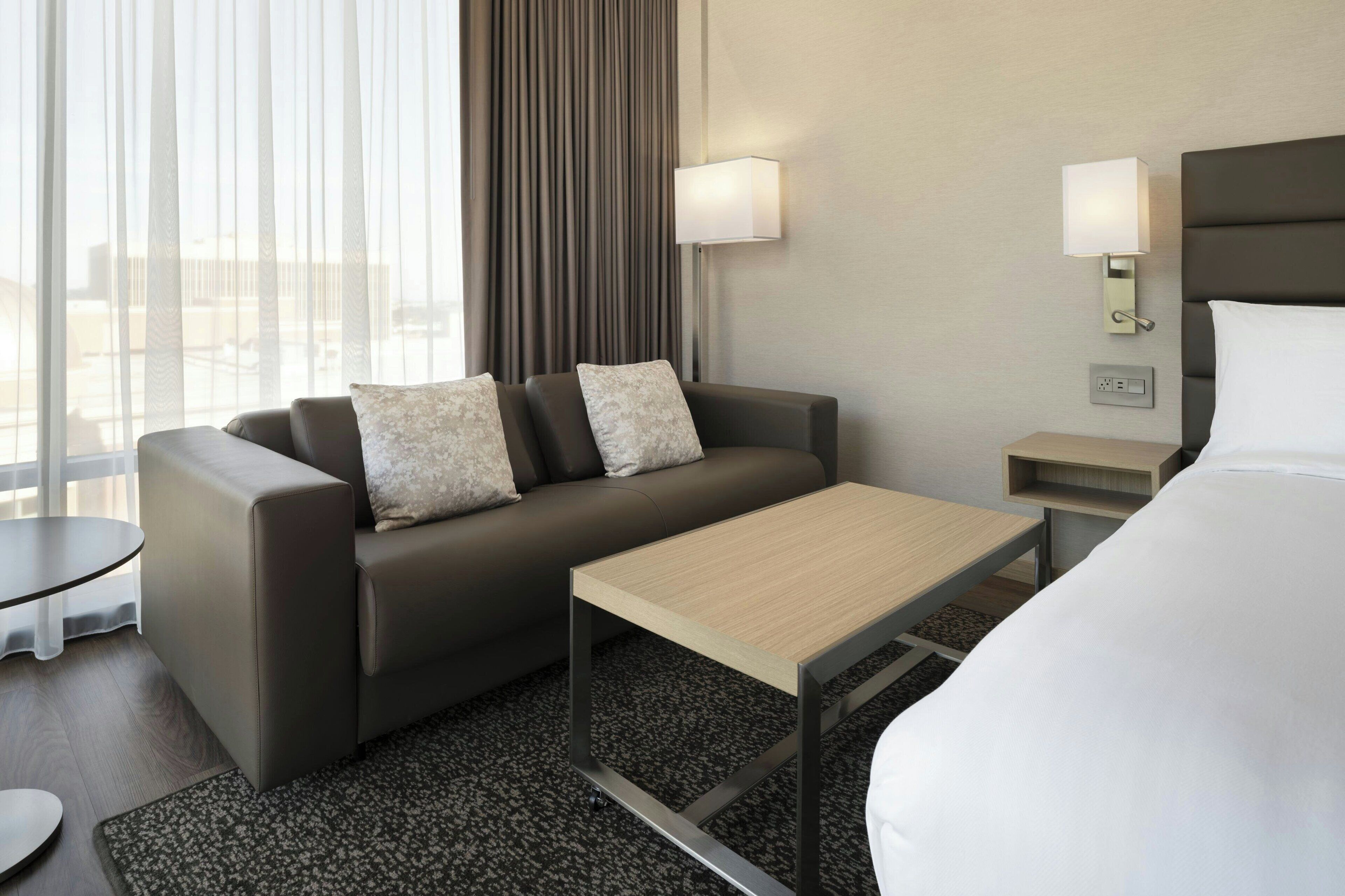 Una habitación de hotel moderna con sofá, una mesita, cama y dos lámparas de pared.