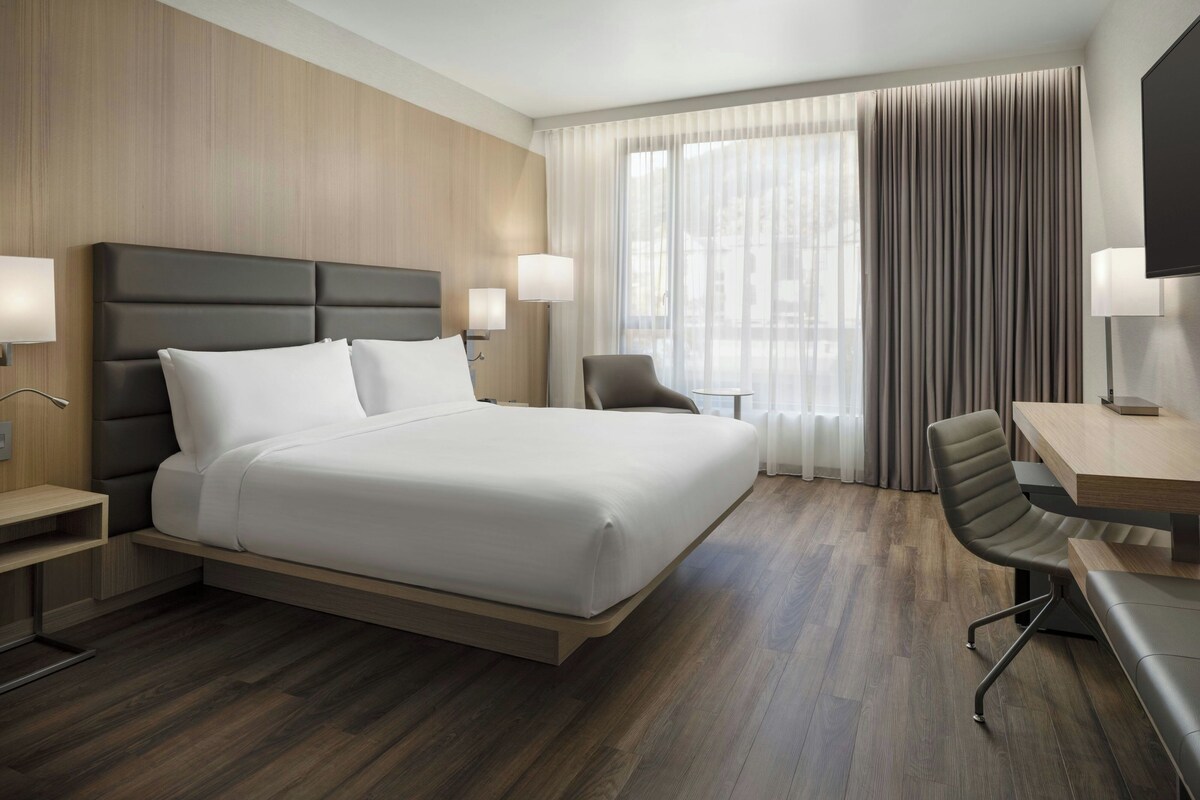 A hotel room with a large bed, a desk, a chair, and a television.