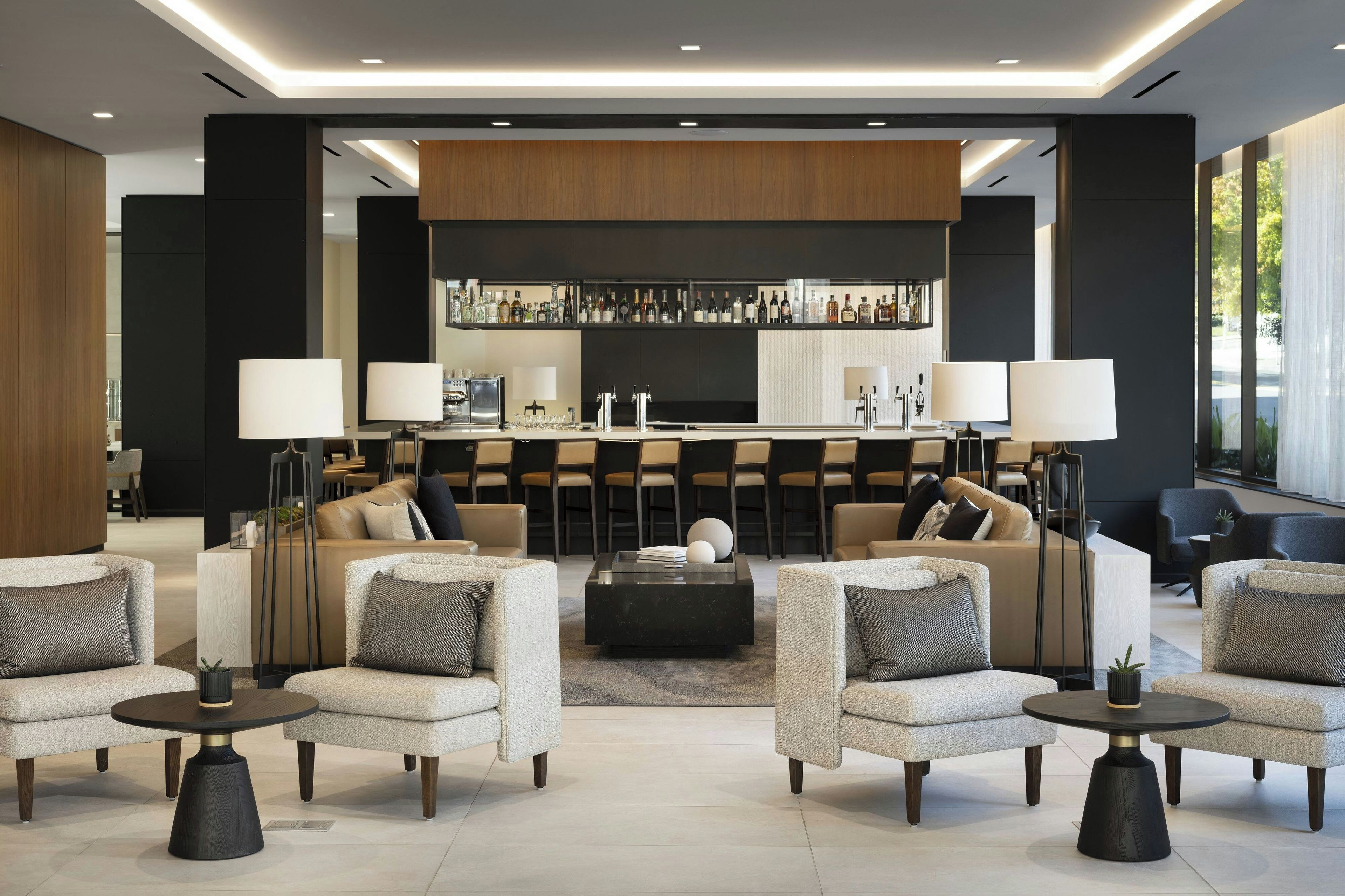 A modern lounge area with sofas, armchairs, a coffee table, and a bar with a variety of bottles.