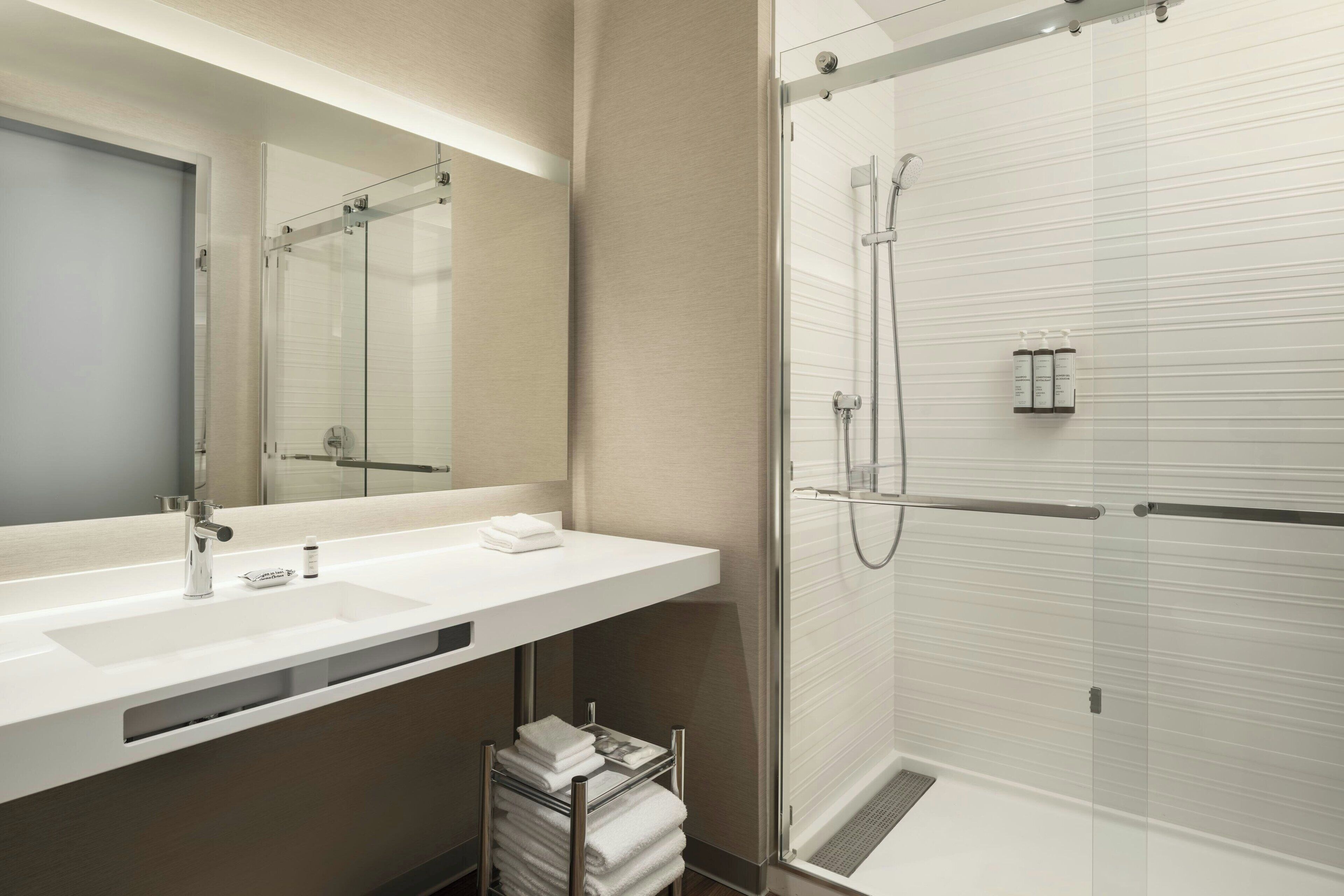 A modern bathroom with a large mirror, white sink, and glass-enclosed shower.