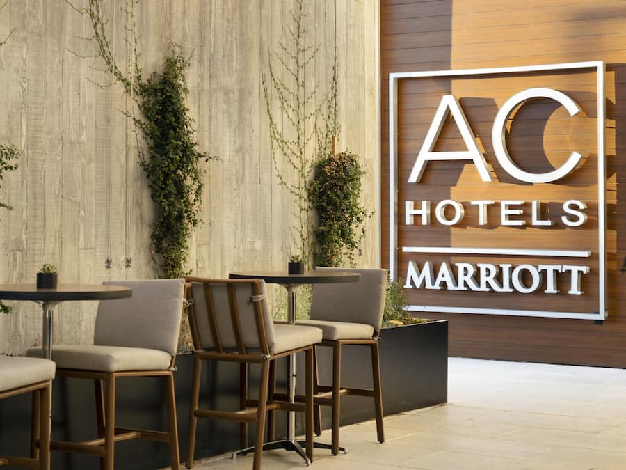 A hotel lobby with a modern design, featuring a large sign for AC Hotels Marriott, comfortable seating, and decorative plants.