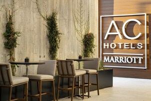 Un vestíbulo de hotel de diseño moderno, con un gran letrero de AC Hotels Marriott, asientos cómodos y plantas decorativas.