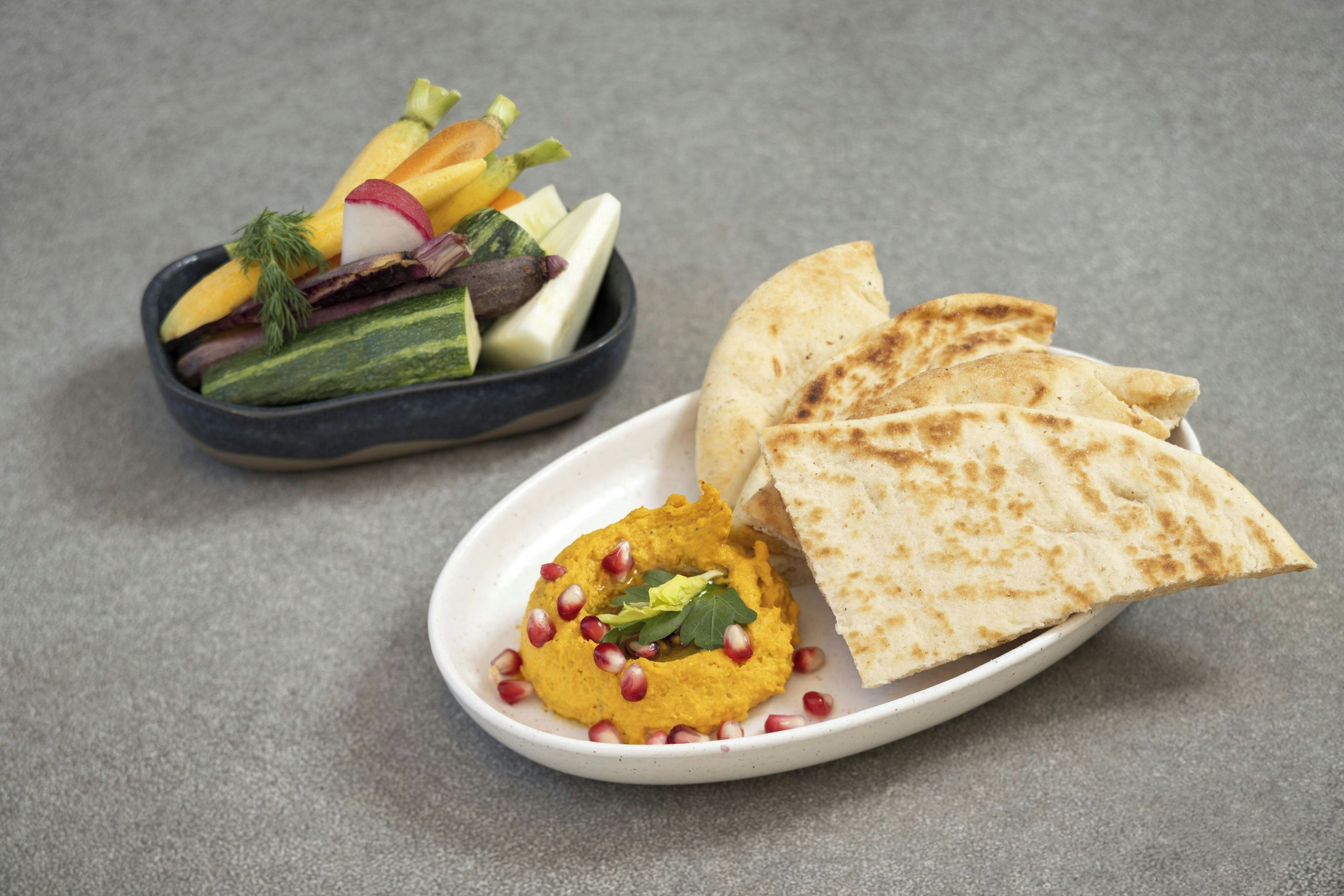 Un plato de hummus y pan de pita, junto con un bol de verduras variadas.