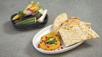 Un plato de hummus y pan de pita, junto con un bol de verduras variadas.