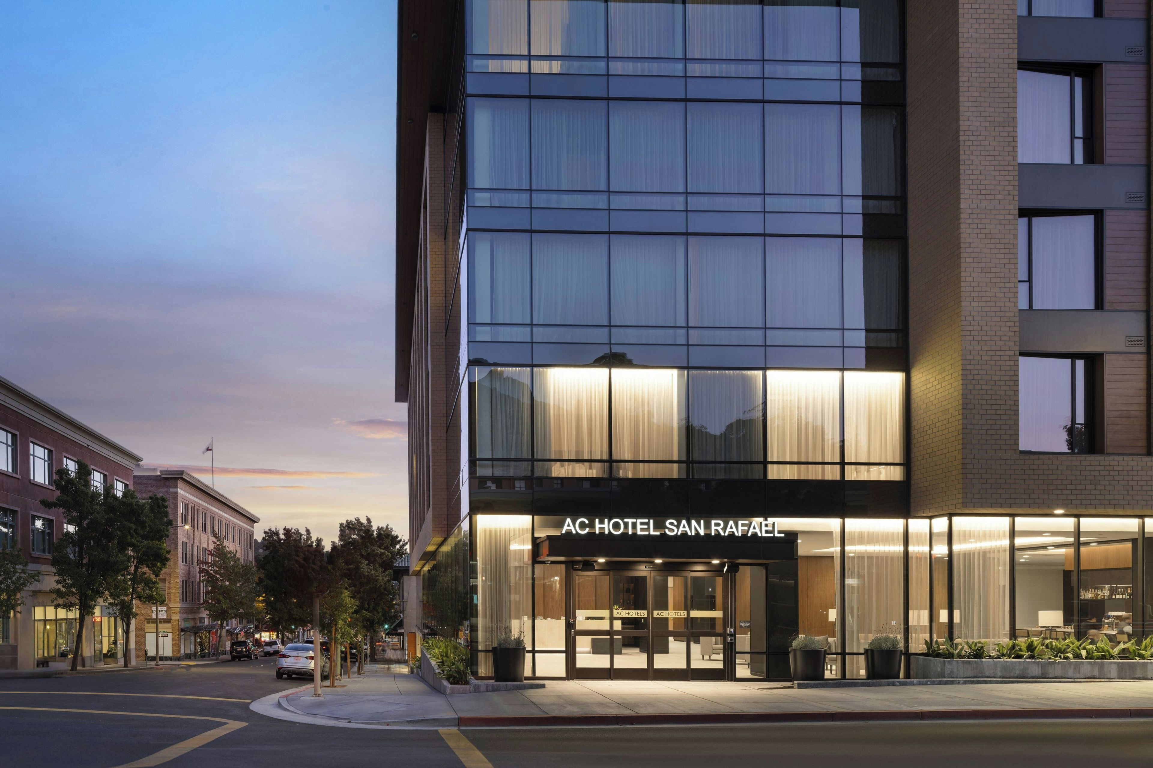 A modern hotel building with a glass facade and a sign reading 'AC HOTEL SAN RAFAEL'.