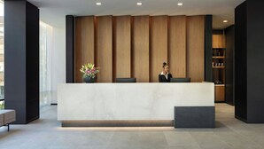 A reception area with a marble counter, wooden paneling, and a receptionist. - AC Hotel San Rafael Downtown (San Rafael)