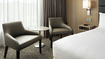 A hotel room with a bed, two armchairs, a small table, a lamp, and a nightstand.