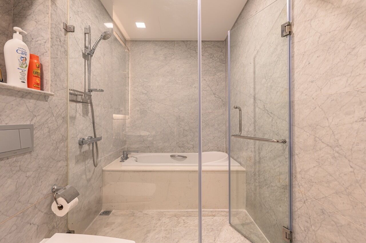 A modern bathroom with a glass-enclosed shower, a bathtub, and marble walls.