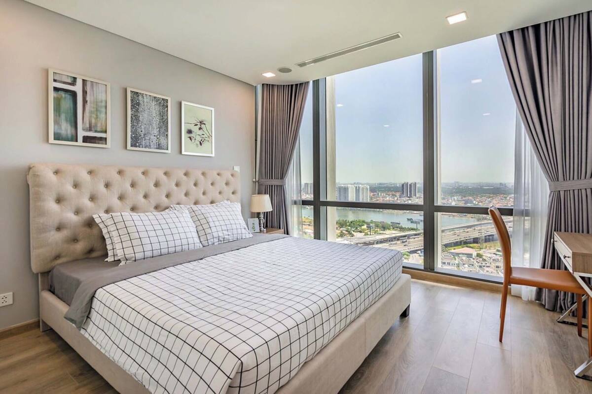 Une chambre moderne avec un grand lit, un bureau et une vue sur le paysage urbain, grâce à de grandes fenêtres.