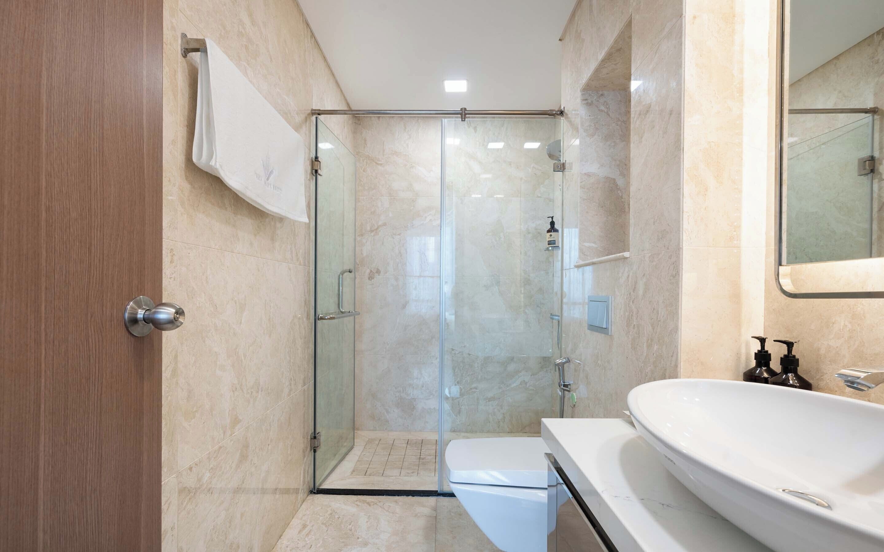 Een moderne badkamer met een douchecabine van glas, een wit toilet en een groot wit wastafelmeubel met een spiegel erboven.