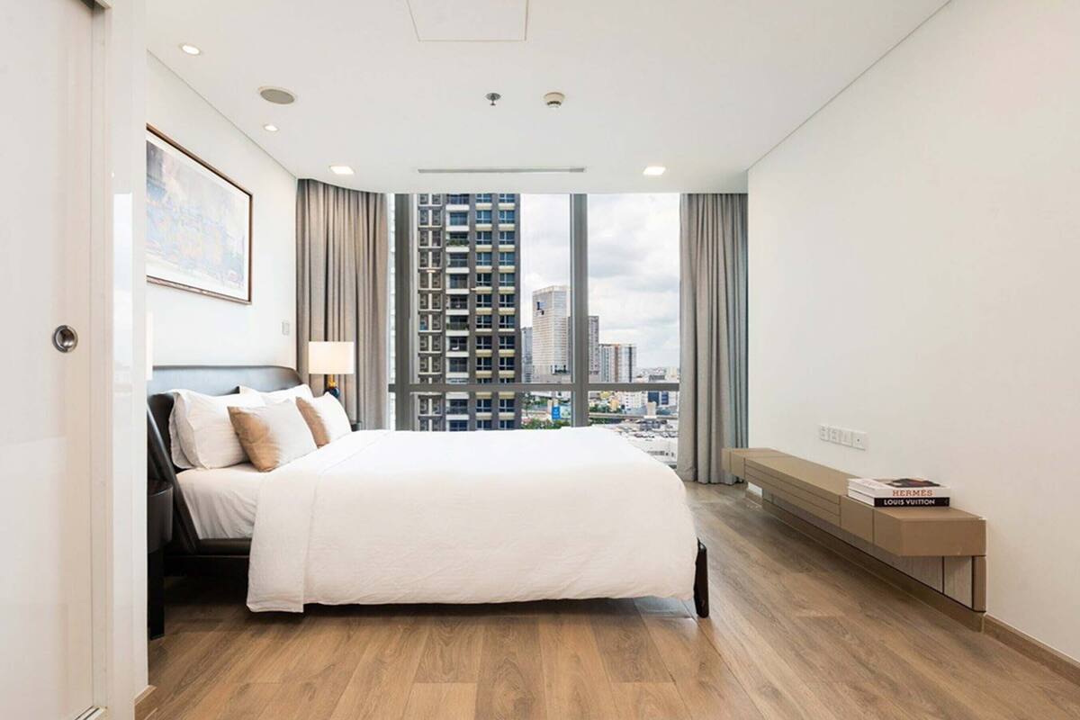 Une chambre d’hôtel moderne avec un grand lit, une table de chevet avec des livres, une vue sur la ville et un plancher en bois.