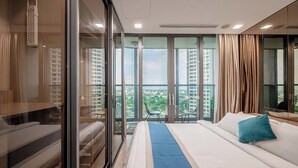 Ein modernes Hotelzimmer mit einem großen Bett, einer Glaskabine und einem Balkon mit Blick auf die Stadt.