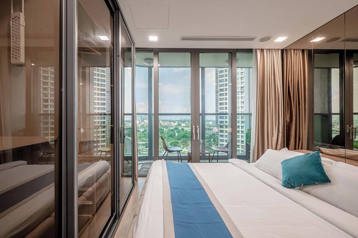 Une chambre d’hôtel moderne dotée d’un grand lit, d’une paroi en verre et d’un balcon offrant une vue sur la ville.