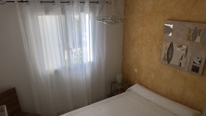 Un dormitorio con cama, una silla, una mesita de noche y una obra de arte colgada en la pared.