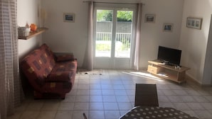 Una sala de estar con sofá, televisión y puerta al balcón.