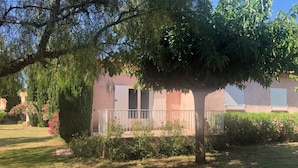 Una casa con un porche cubierto, césped y un árbol grande en primer plano.