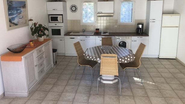 Una cocina compacta con armarios blancos, una mesa de comedor con cuatro sillas y piso de baldosas.