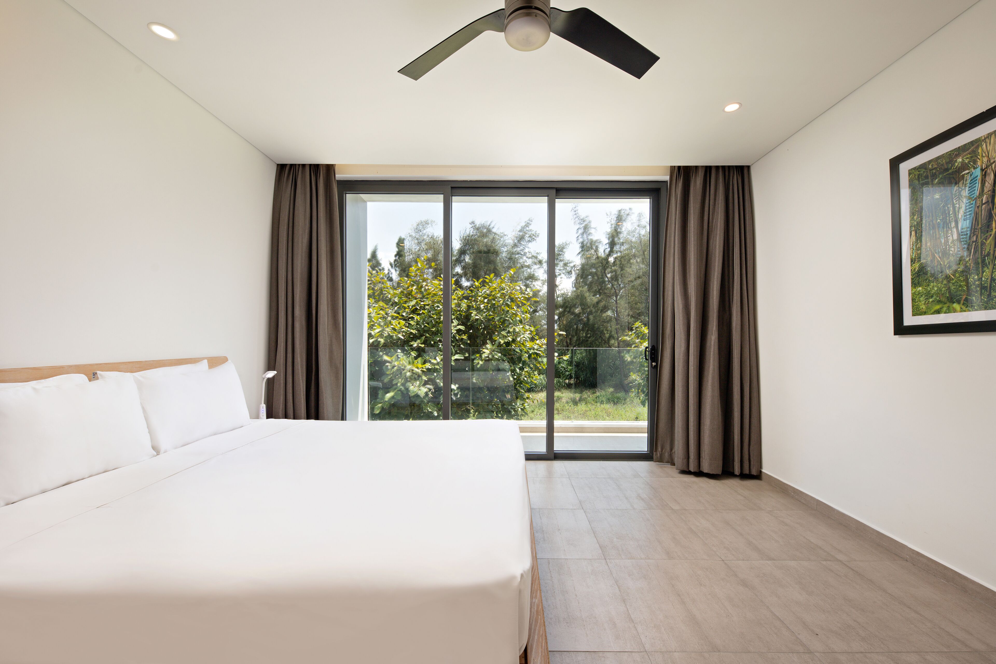 Ein modernes Schlafzimmer mit einem großen Bett, einem Deckenventilator und einer Glasschiebetür, die zu einem Balkon führt.