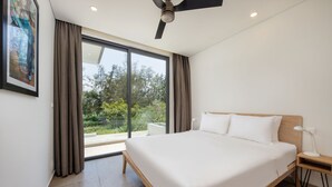 A modern bedroom with a large bed, a ceiling fan, a nightstand with a lamp, and a view of greenery outside. - The Point Villa Da Nang (Da Nang)