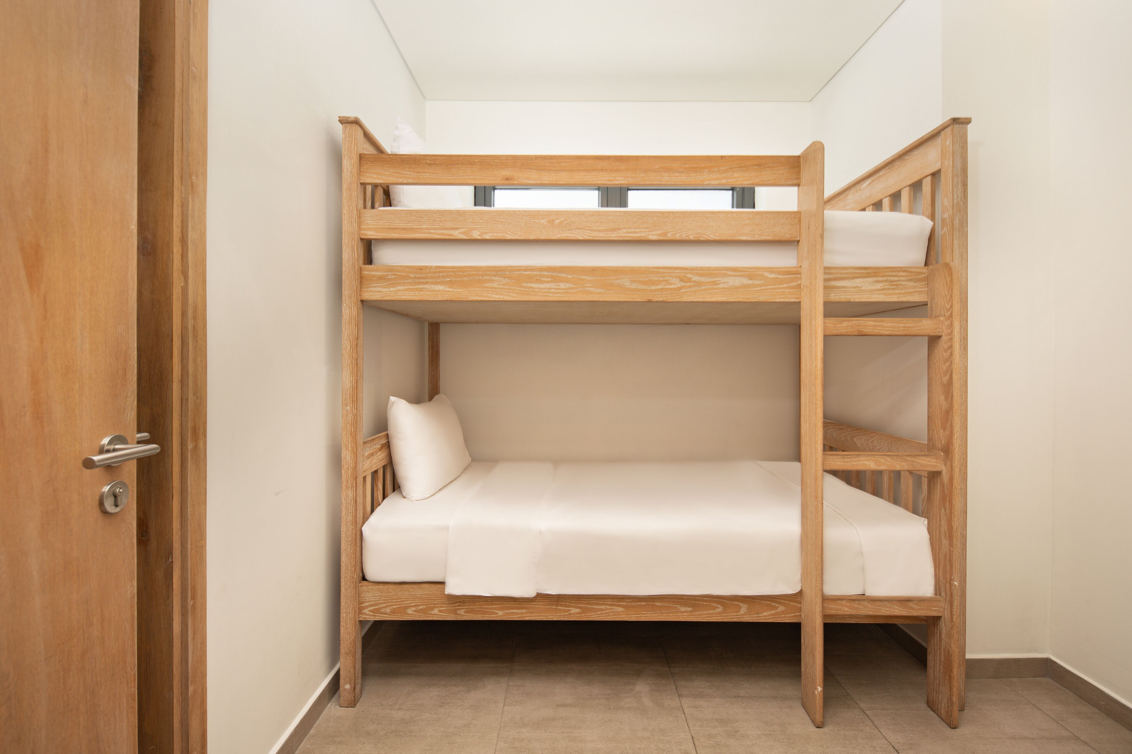 A bunk bed in a room with a wooden door and a tiled floor.