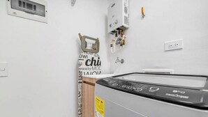 A laundry room with a front-loading washing machine, a wall-mounted heater, and a towel rack.