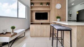 A modern kitchen with a built-in TV, wooden shelves, a clock, and a bar area.