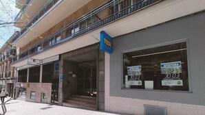 Un edificio con escaparate, un cartel que dice 'TEDI' y un escaparate que muestra un anuncio de 'APERTURA' con la hora 30:03.