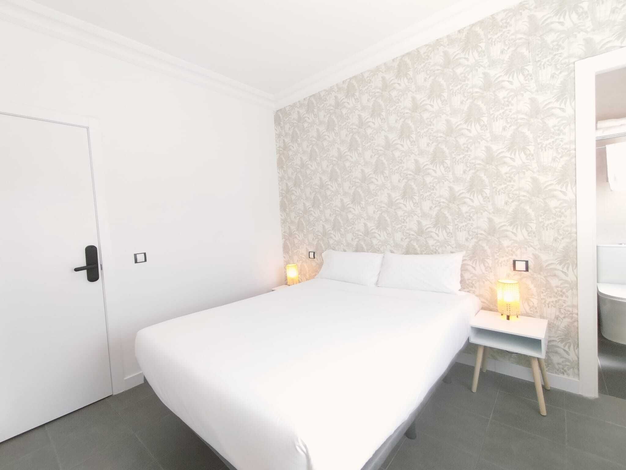 Un dormitorio con una cama grande, dos mesitas de noche con lámparas, un armario y un papel tapiz estampado.