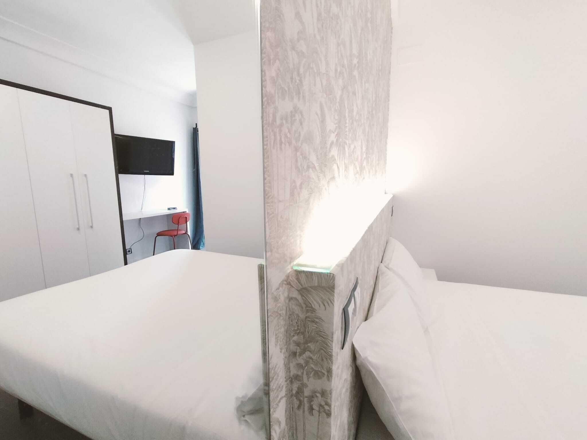 A hotel room with a bed, a desk with a chair, and a wardrobe.