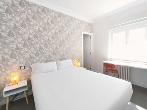 Un dormitorio con cama, escritorio y silla. Una ventana proporciona luz natural.