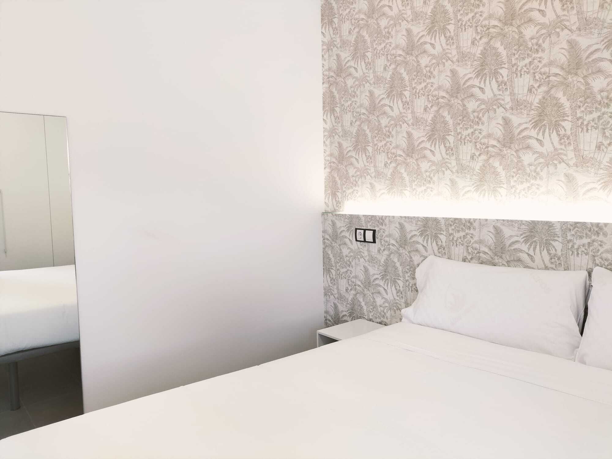 A hotel room with a bed, a nightstand, and a mirror.