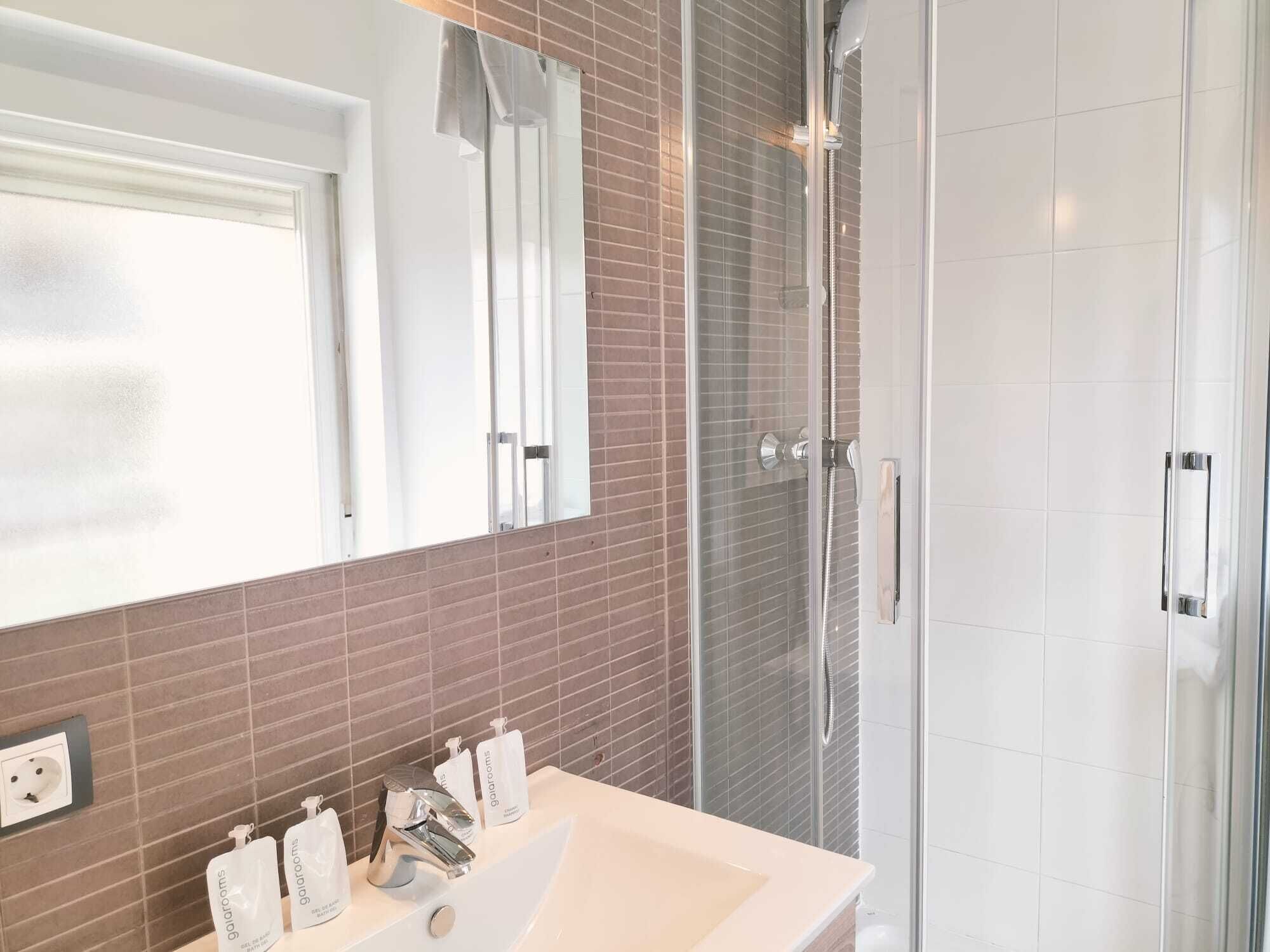 A modern bathroom with a glass shower enclosure, a white sink, and a mirror above it.
