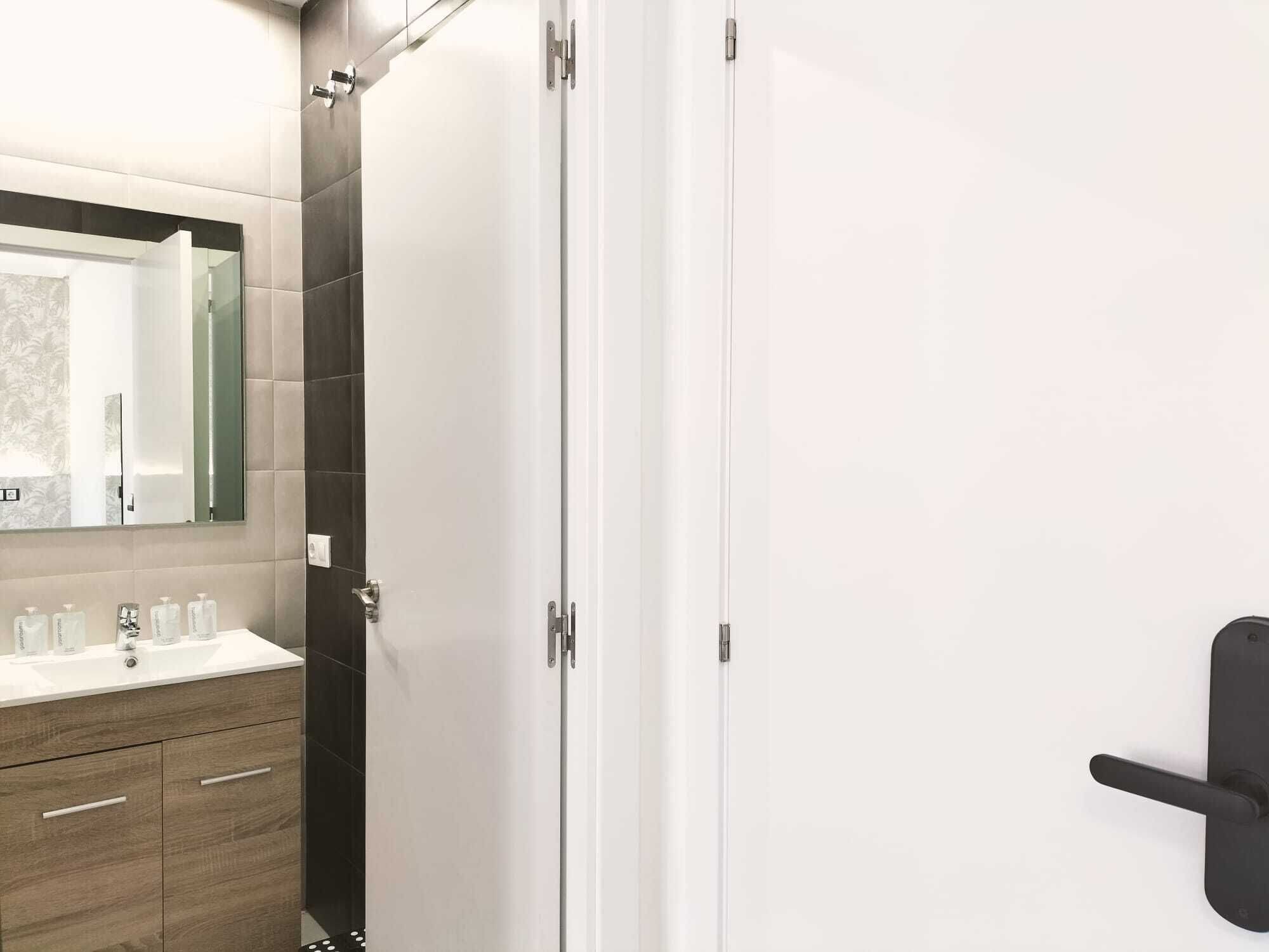 Un baño moderno con tocador blanco, baldosas oscuras y pomo negro.