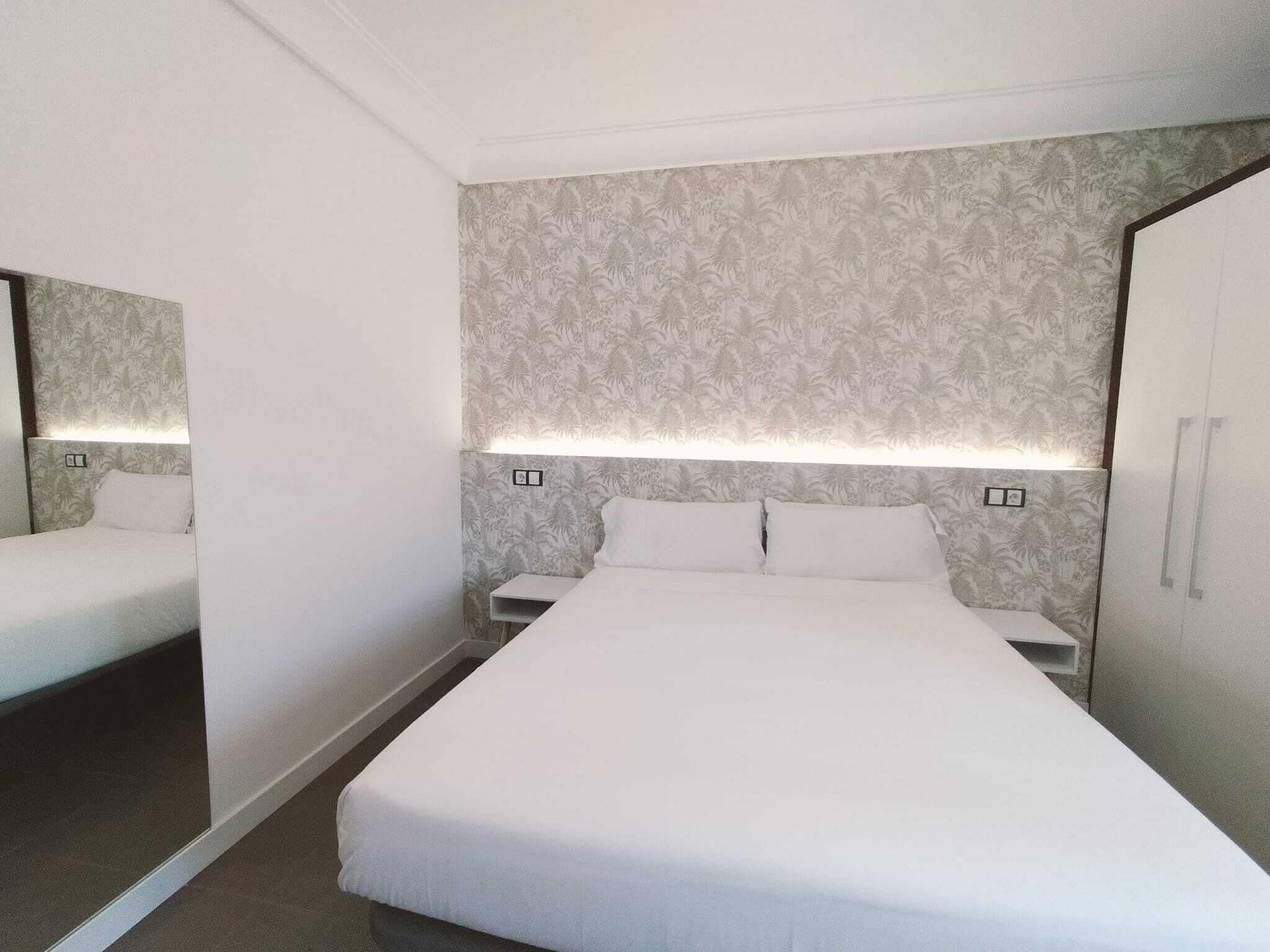 A hotel room with a large bed, two bedside tables, and a wardrobe.