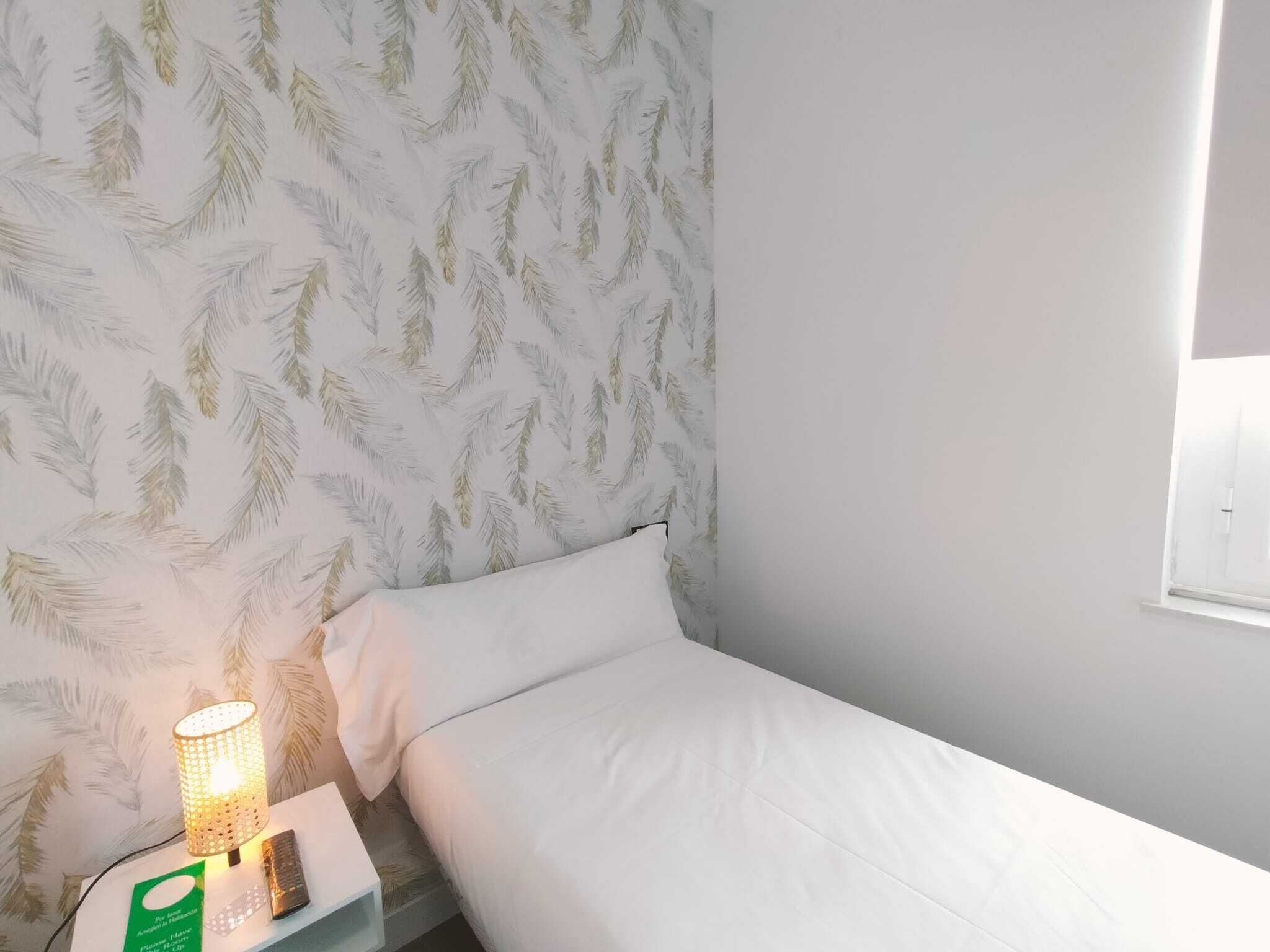 A bedroom with a bed, a nightstand, a lamp, and a window.