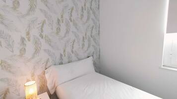 A bedroom with a bed, a nightstand, a lamp, and a window.