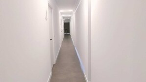 Un pasillo estrecho y bien iluminado con paredes blancas y piso alfombrado, que conduce a una puerta al final.