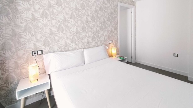 Un dormitorio con cama, mesitas de noche, lámpara y una puerta.