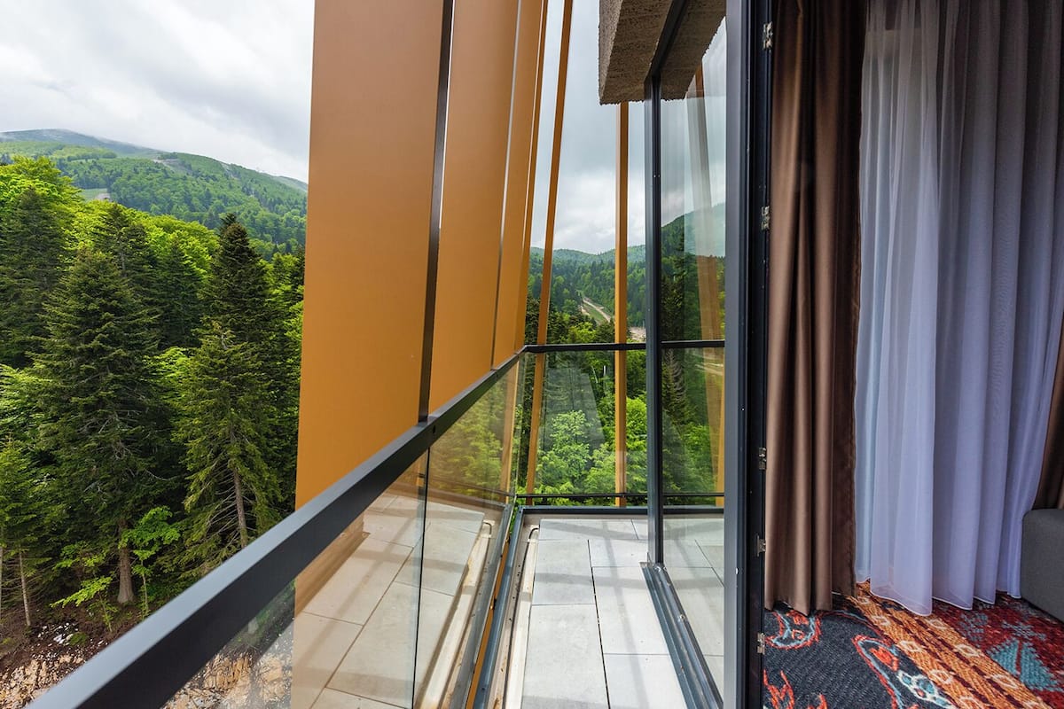 Een balkon met glazen hekwerk met uitzicht op een bebost berglandschap.