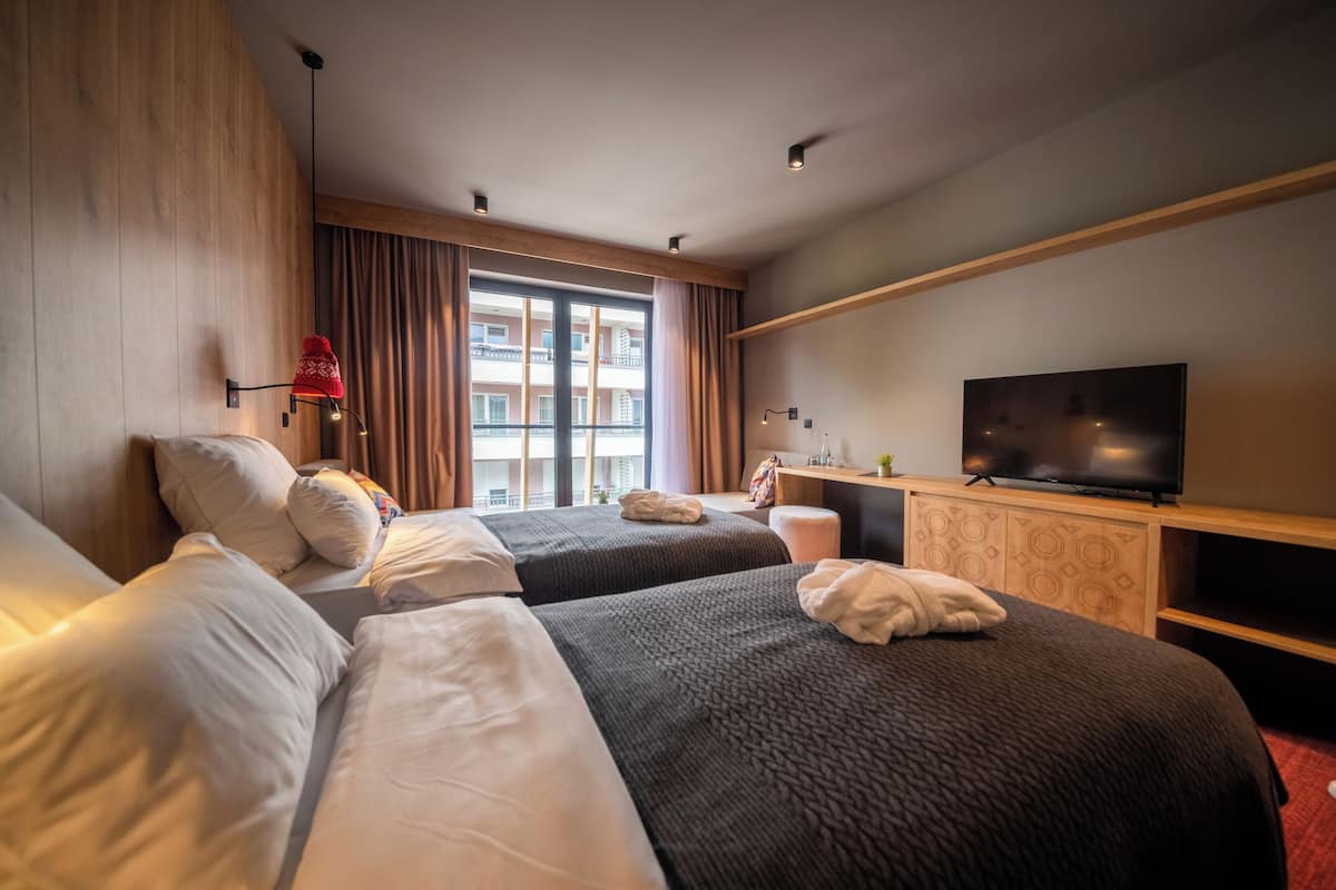 Een hotelkamer met twee bedden, een televisie, een bureau en een raam met gordijnen.