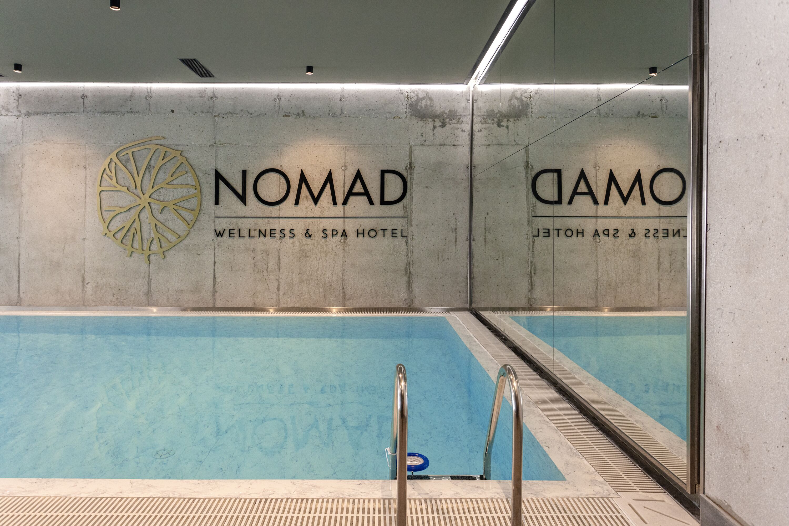 A swimming pool area with a NOMAD WELLNESS & SPA HOTEL sign.