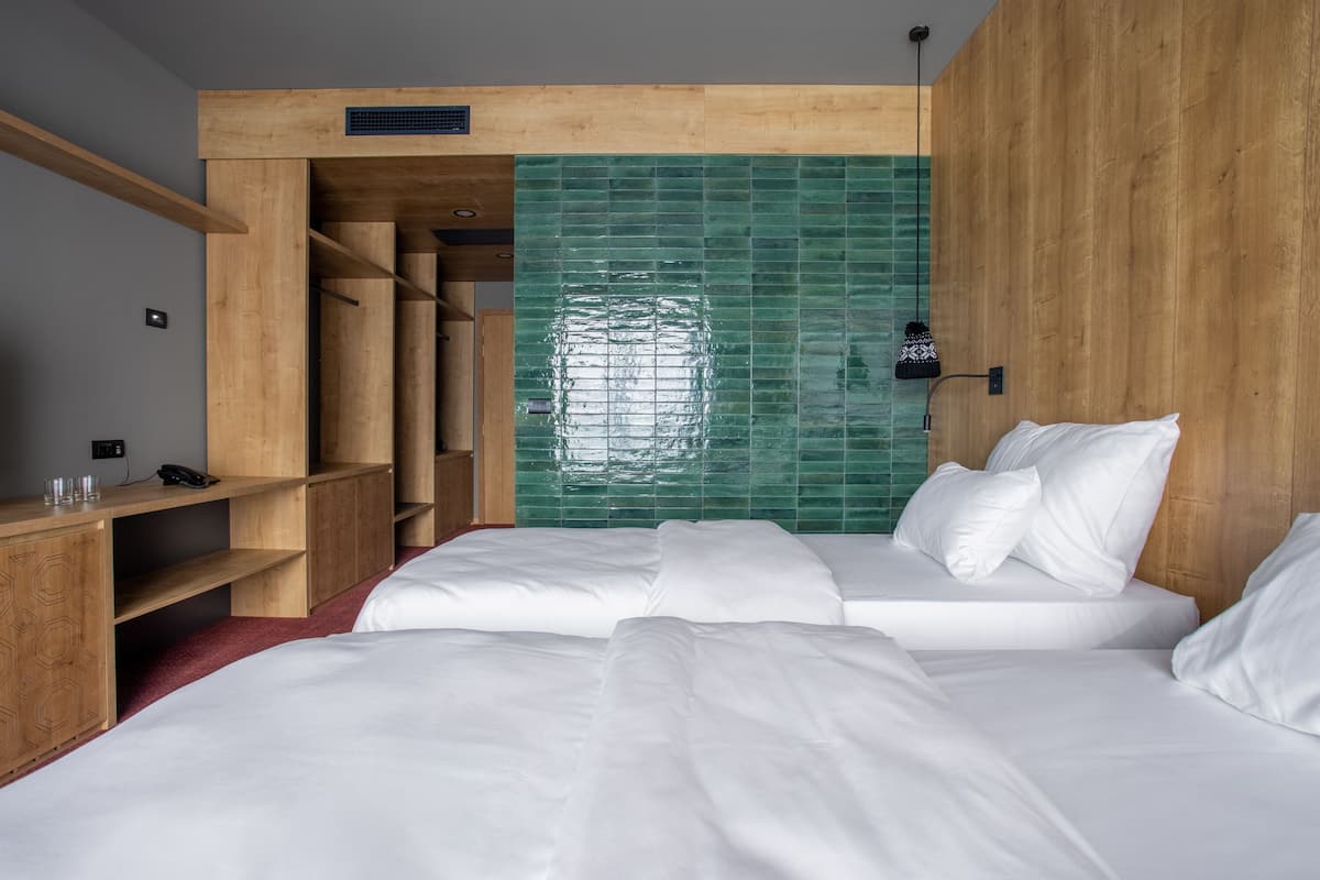 Een hotelkamer met een houten hoofdbord, een accentmuur betegeld met groene tegels, en een bed met witte lakens.