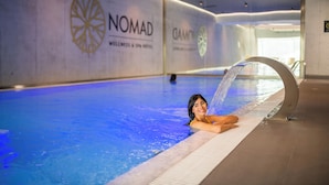 A swimming pool with a water feature, surrounded by walls with 'Nomad Wellness & Spa Hotel' branding.