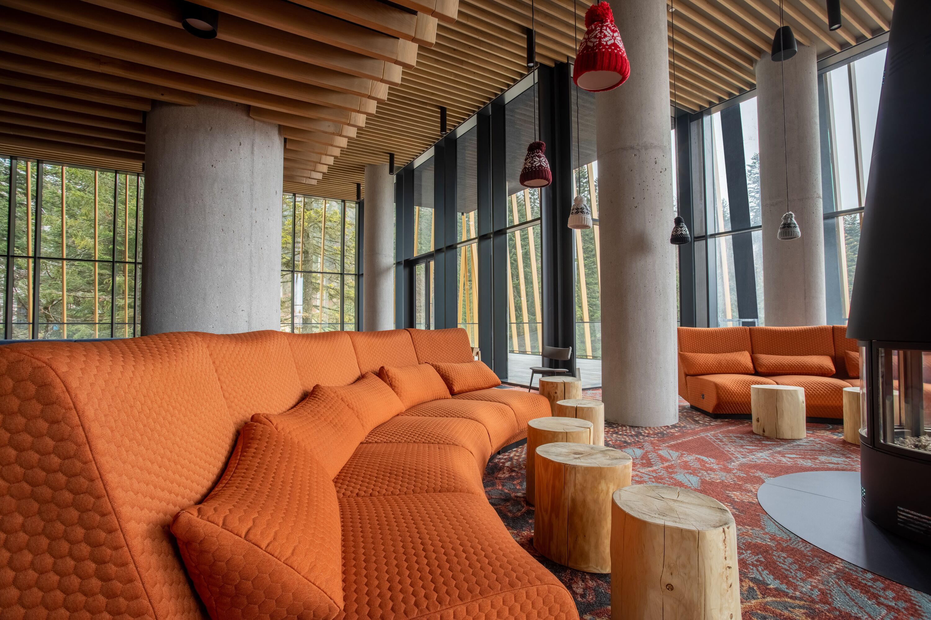 Um interior moderno com um amplo sofá de canto laranja, tabouretos de madeira e grandes janelas que oferecem iluminação natural.