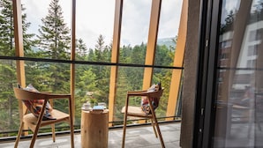 A balcony with two wooden chairs and a small round table, overlooking a forested area.