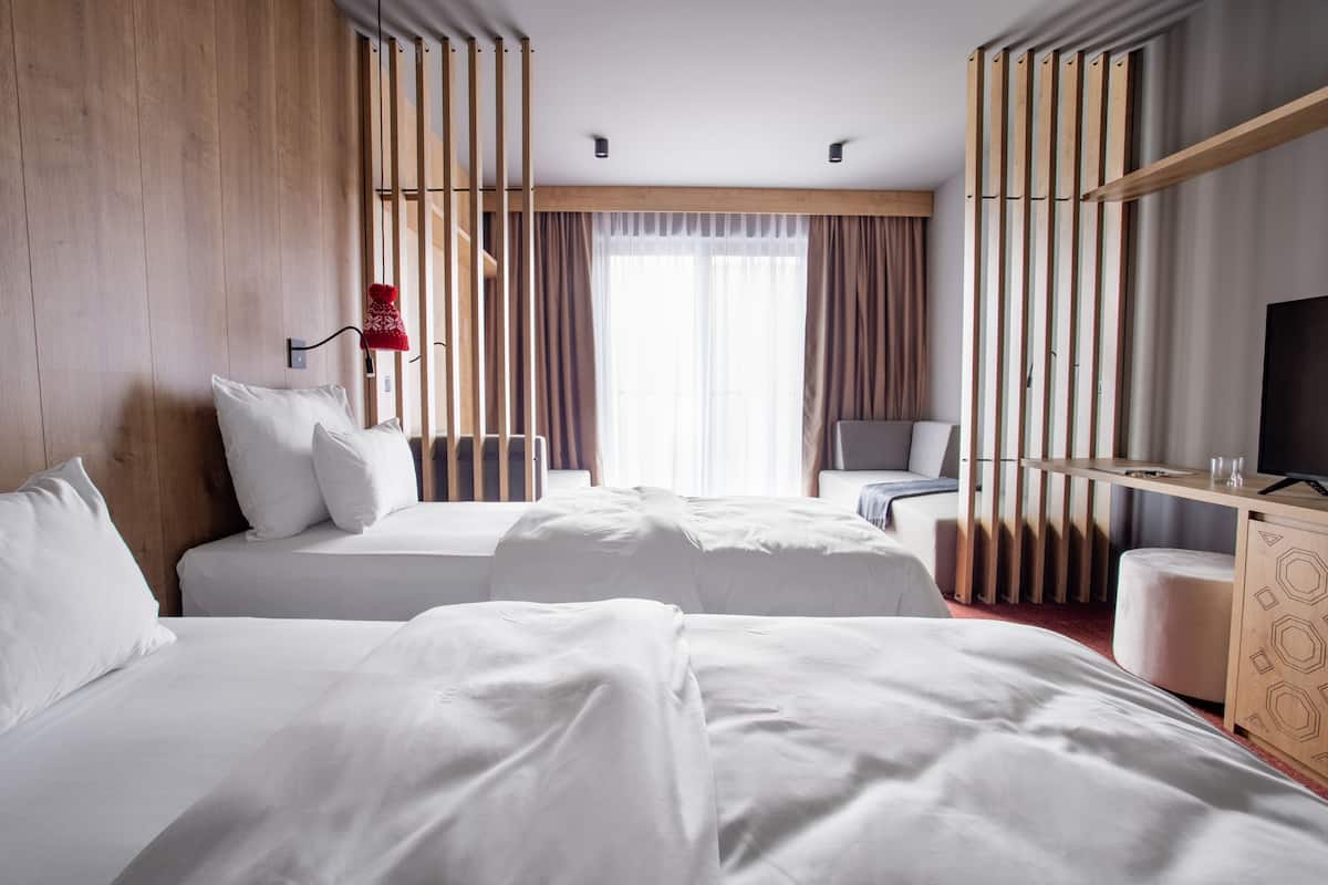 Een hotelkamer met twee bedden, een bureau, een televisie en een raam met gordijnen.