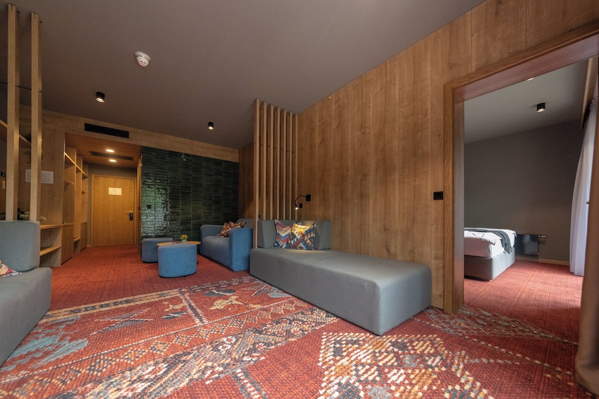 Een moderne hotelkamer met een ruime zithoek, een kamerbreed tapijt met dessin en een houten accentmuur.