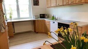 A kitchen with wooden cabinets, a microwave, a dishwasher, and a window with blinds. - Tastefully furnished vacation apartment "Landidylle" (Stemwede)