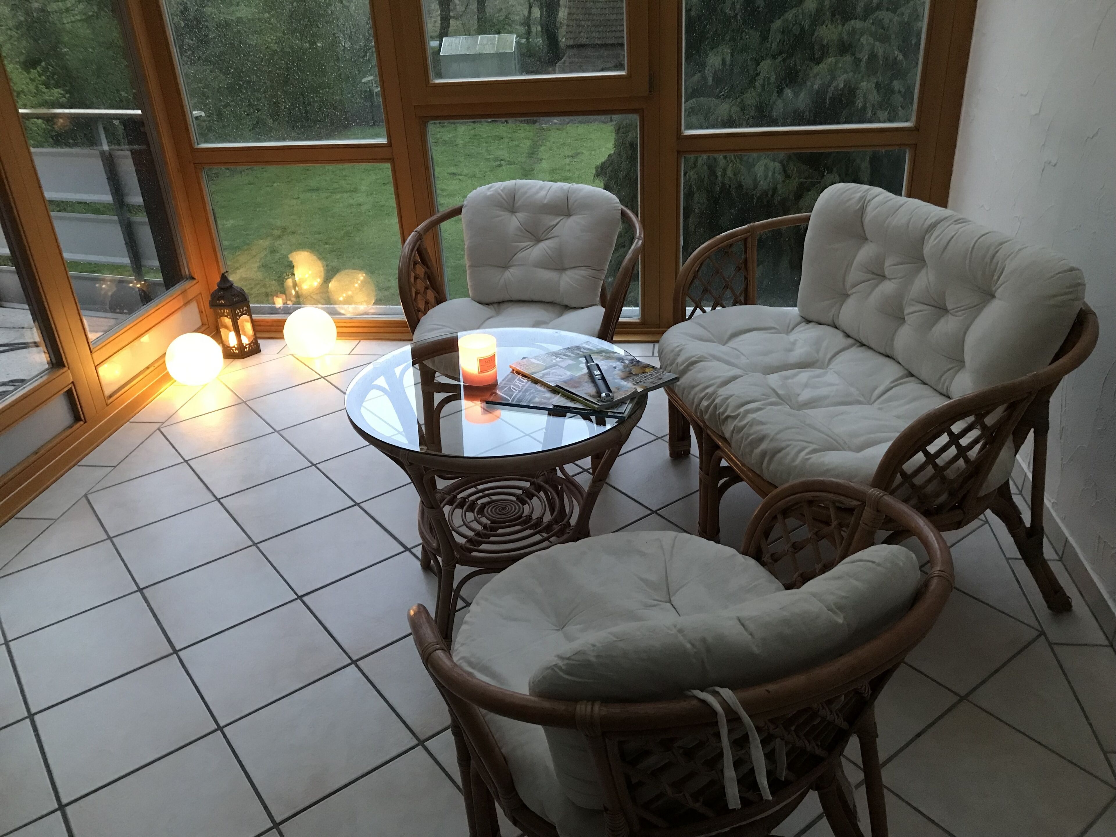 Un coin salon accueillant avec des fauteuils en osier et une table en verre, agrémenté d’une bougie et d’un livre.
